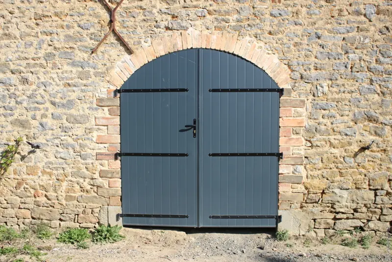 Volets battants aluminium FPEE Anna gris anthracite sur une ouverture cintrée en pierre
